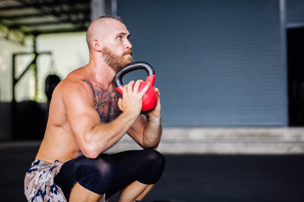 Exercice kettlebell boxe : un homme fait un squat avec un kettlebell